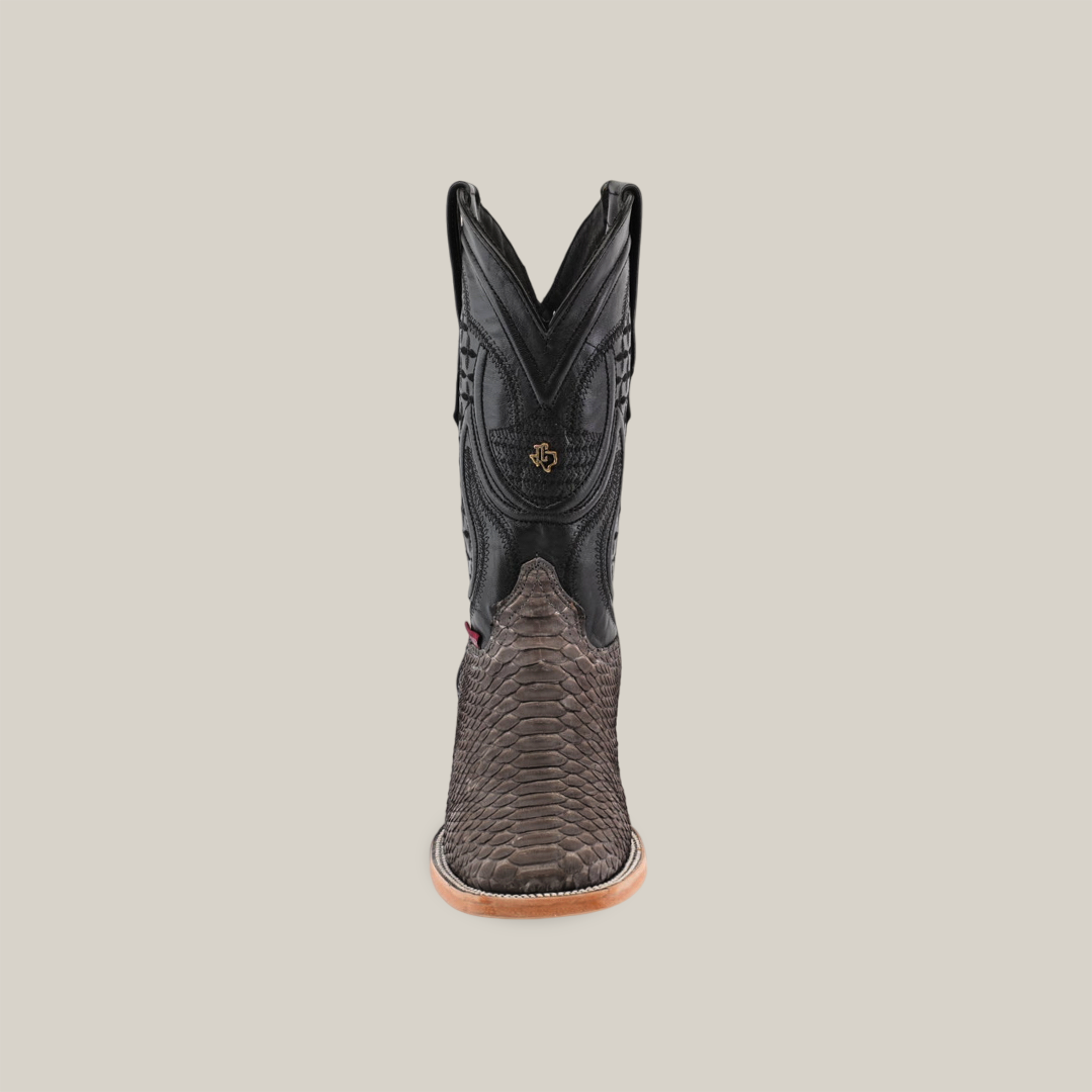 The Exotic Python - Matte Gray is a single square toe cowboy boot showcasing intricate stitching and a decorative emblem. It features a black upper, textured brown leather lower, and tan sole, all set against a plain light beige background.