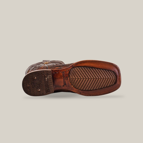 Bottom view of the Exotic Python - Rustic Cogñac cowboy boot highlights its square toe and tread pattern. Engraved brand logo on the heel, with intricate stitching and textured grip on the sole. Styled in rich cognac, set against a plain background.