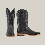 A pair of Exotic Caiman Horn Back boots in black with intricate stitching and a wooden heel, one boot front-facing and the other side-facing, set against a plain beige background.