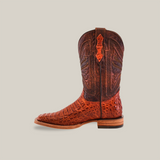 The Exotic Caiman Horn Back - Brandy boot flaunts textured, crocodile-like Caiman leather on the foot with intricate stitching on the shaft, all set against a neutral backdrop. It features a square toe and a wooden heel.