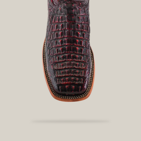 A close-up of the Exotic Caiman Horn Back boot in Black Cherry shows its textured alligator pattern. Crafted with high-quality caiman leather, it features a broad square toe, intricate stitching, and a light brown leather outsole against a simple light beige background.