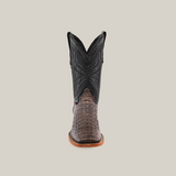 The Exotic Caiman Horn Back - Serpentine boot features a forward-facing black upper with intricate stitching, a textured brown lower made of genuine caiman leather, and a light brown sole. It is displayed against a plain beige background.