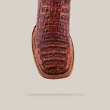 Close-up of the Exotic Caiman Horn Back - Smoke Cogñac boots square toe, featuring textured red-brown caiman leather with a reptile skin pattern. Handcrafted stitching enhances the look, casting a subtle shadow on a light background.