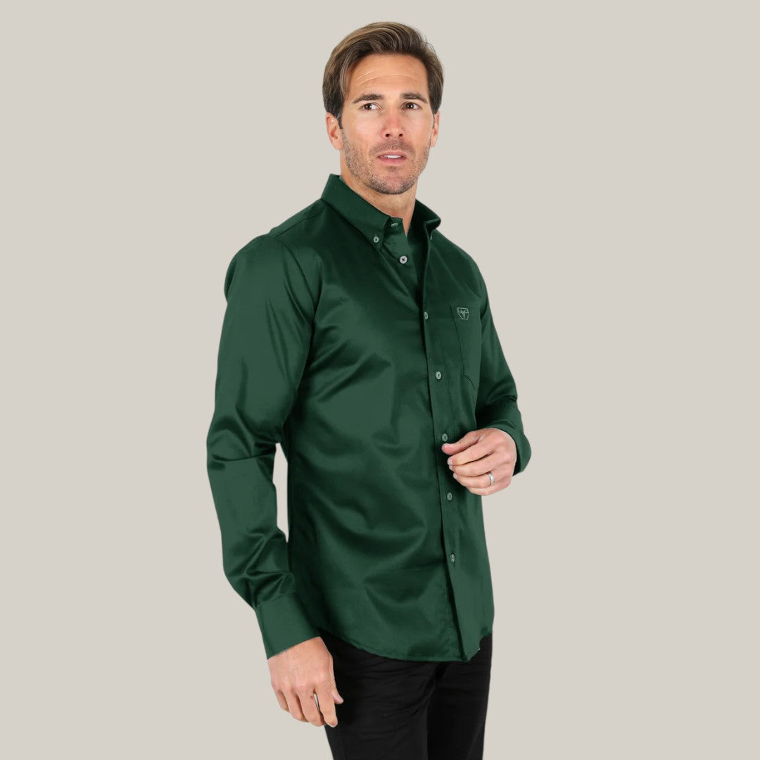 Against a light gray background, a person stands slightly turned, wearing the mens modern fit stretch dress shirt in dark green (Product: CTL9667) and black pants; it has a subtle logo on the chest pocket.