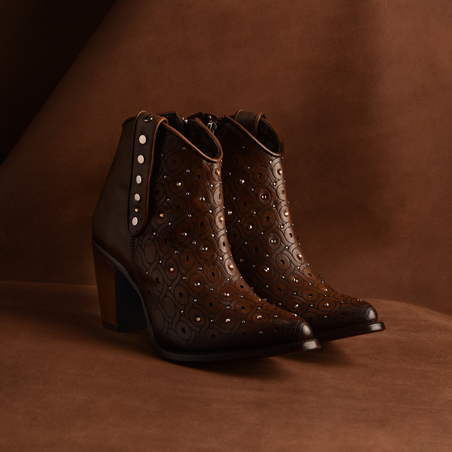 The Maple Laser & Crystals & Studs - Round Toe ankle boots feature brown leather with laser details, metal studs, a chunky heel, and side zippers, all set against a matching brown background to blend style and craftsmanship.