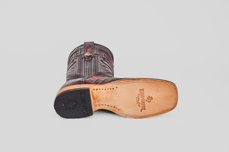 A single Exotic Caiman Horn Back - Black Cherry - Square Toe boot lies on its side, revealing the tan leather sole with the Texas Signature logo, black heel, and decorative stitching on dark leather. The background is plain light gray.