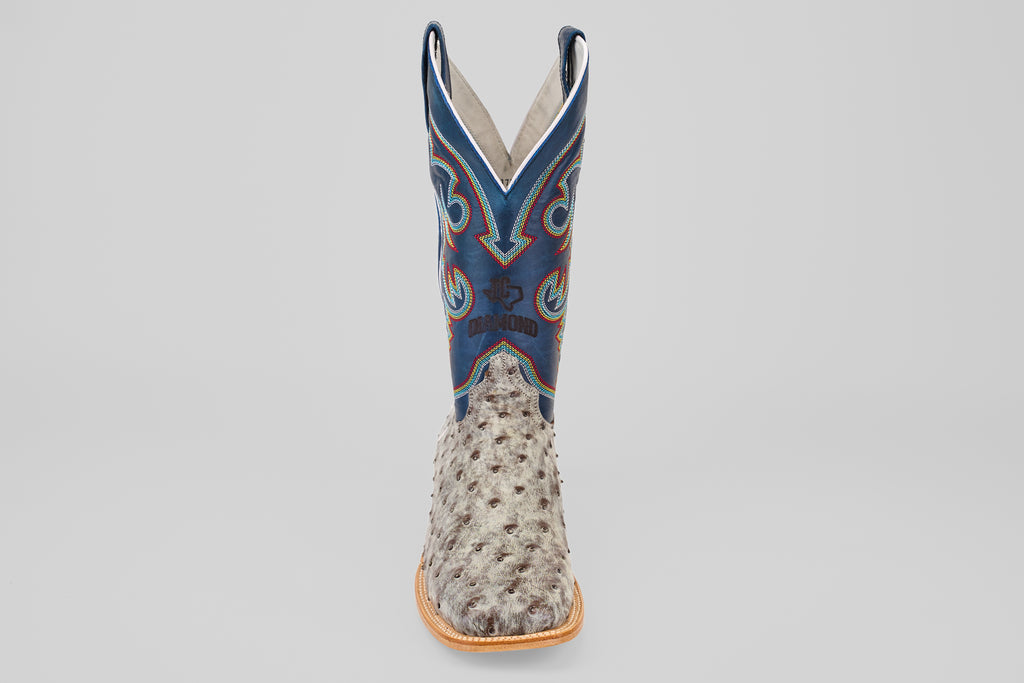 A single Russell - Rustic Gray - Square Toe Western boot with a light brown ostrich leather foot, blue shaft, decorative stitching, and tan sole is shown facing forward against a plain light background.