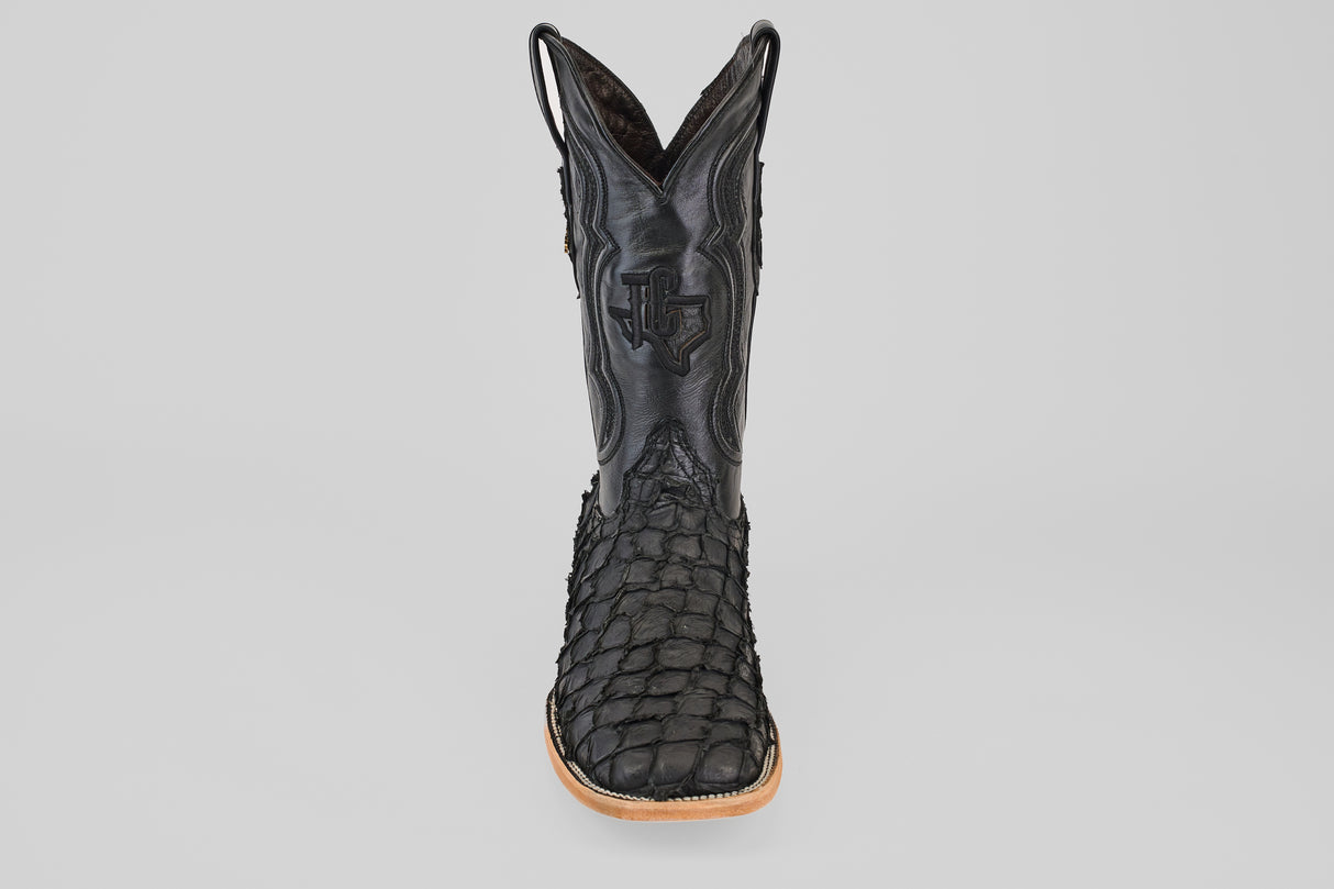 A single Exotic Pirarucu Fish - Matte Black - Square Toe boot, featuring textured leather and a tan sole, is shown upright and facing forward against a plain gray background.