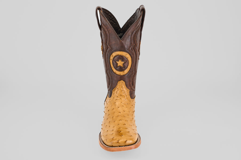 The Exotic Full Quilt Ostrich - Fawn - Square Toe boot features a tan ostrich foot, dark brown shaft, and a star emblem patch, offering timeless cowboy style with premium craftsmanship.