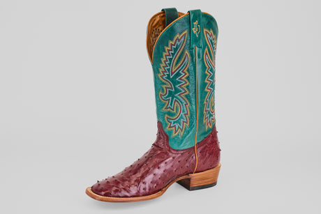 The Rusty - Wine - Square Toe cowboy boot showcases a wine ostrich leather foot, tall teal shaft with detailed yellow, blue, and red stitching, and a wooden heel, all set against a plain white backdrop.