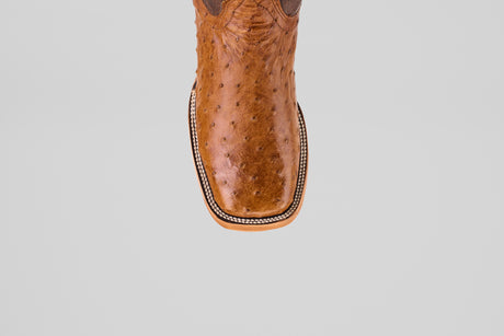 A top view of the Exotic Full Quilt Ostrich - Brandy Brucciato boot features brown leather, a square toe, and decorative edge stitching in classic cowboy style, set against a plain light gray background.