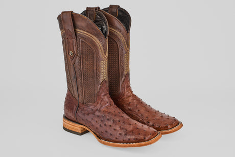 The Exotic Full Quilt Ostrich - Brown - Square Toe boots feature textured ostrich leather, decorative shaft stitching, and light wooden heels, displayed against a plain gray background.