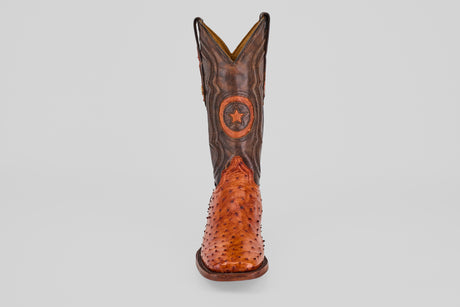 The Austin - Brandy - Square Toe features a single brown cowboy boot with a textured Avestruz Brandy leather foot, dark shaft, and circular star emblem on the front, shown against a plain light background.