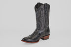 The Tanner - Black - Round Toe is a single black leather cowboy boot with intricate shaft stitching and a Python Negro Oval patterned foot, featuring a brown stacked heel and sole, displayed on a plain light gray background.