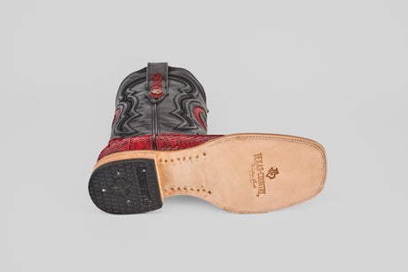 A single Tanner - Ruby - Square Toe boot with a black and red Python Rojo design rests on its side, showcasing the tan leather sole stamped with the Texas Country Genuine logo and a textured black heel.