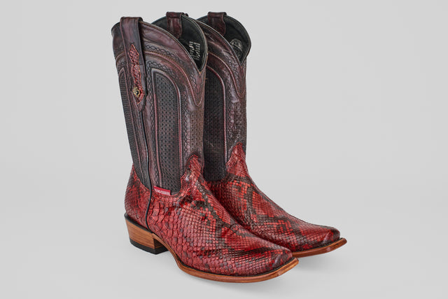 The Tanner – Ruby – Narrow Square Toe boots, featuring red and brown snakeskin, detailed shaft stitching, and light brown wooden heels, are shown against a plain light gray background.
