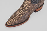 Close-up of the snip toe and upper of the Tanner – Rustic Bone boot, crafted from textured, patterned brown python leather with a wooden sole and black trim, set against a plain light background.