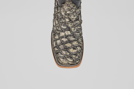 A close-up of the Conor - Rustic Bone - Square Toe men's cowboy boot shows its textured fish leather pattern in brown and tan, with detailed stitching along the sole edge.