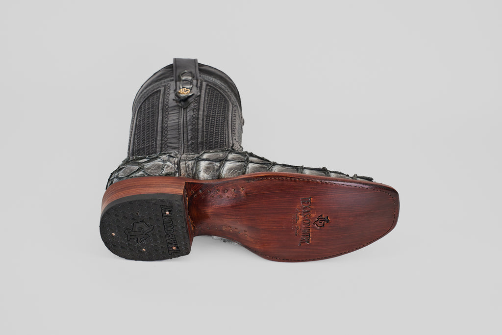 The Conor - Newspaper - Narrow Square Toe cowboy boots, one upright and one on its side, display detailed leather textures and patterned soles, with a narrow square toe and visible branding on the sole.