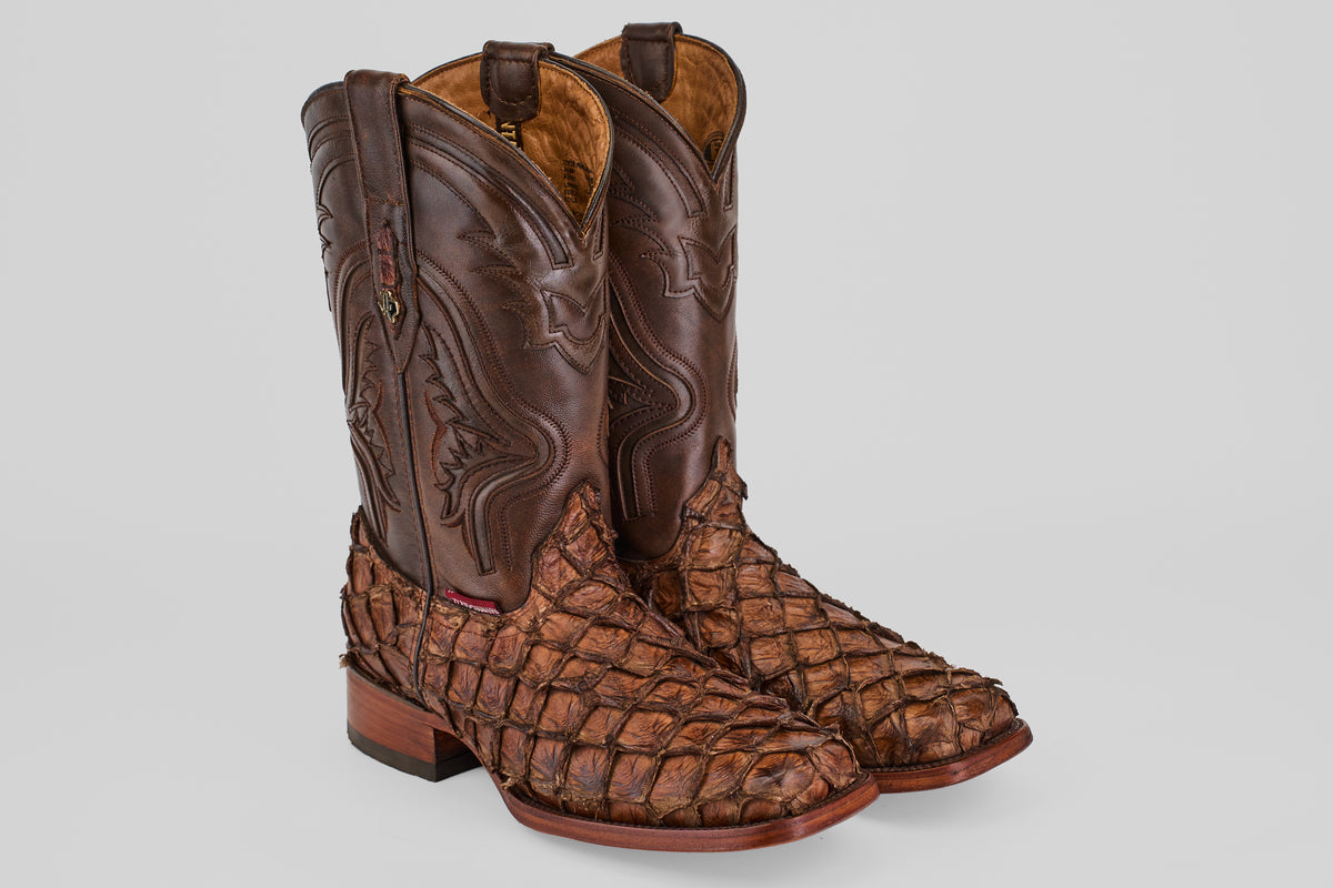 The Conor - Brown - Rodeo Toe boots feature intricate shaft stitching and textured pirarucu leather on the feet, shown against a light gray background.