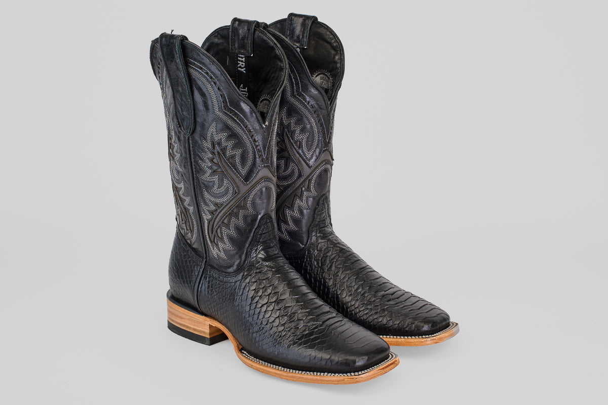 The Python Black - Embossed Leather - Square Toe (E425) boots feature a black textured finish, intricate stitching on the shaft, and light brown leather soles, showcased on a neutral gray background.