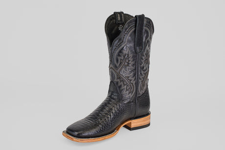 The Python Black - Embossed Leather - Square Toe (E425) is a single black cowboy boot featuring intricate stitching, a textured lower pattern, and a light brown wooden sole, photographed against a plain gray background.