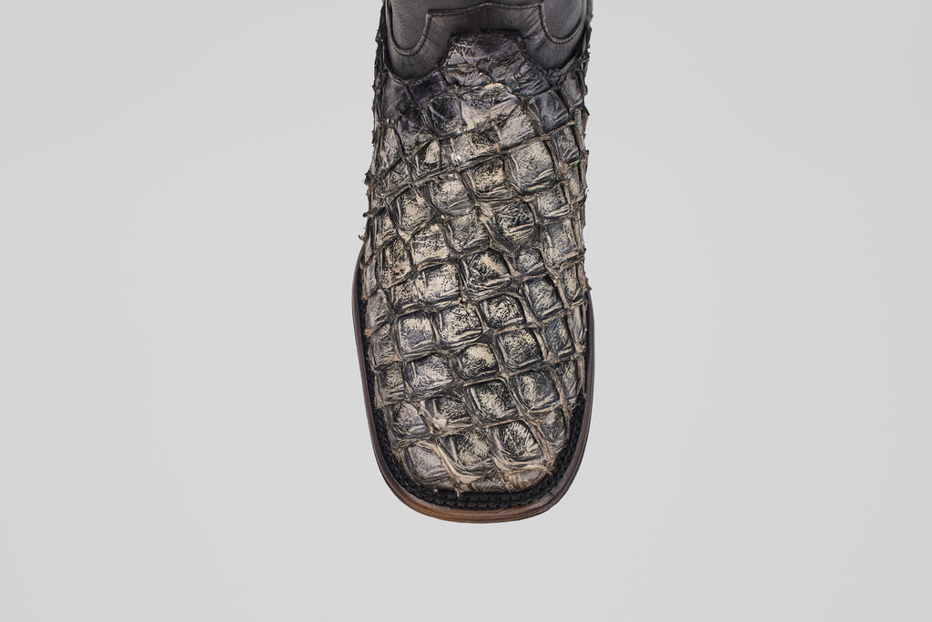 A close-up of the Conor Platinum - Newspaper - Square Toe (Diamond) cowboy boot, featuring dark, textured crocodile-patterned leather and a brown edge, displayed against a plain white background.