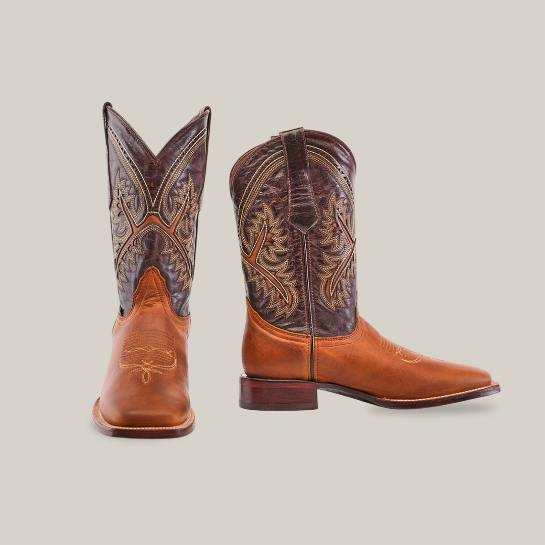 A pair of Cater Honey - Square Toe boots in premium cowhide feature intricate stitching. The right boot stands upright as the left angles outward, showcasing a blend of brown leather with darker upper patterns, reflecting artisan craftsmanship.