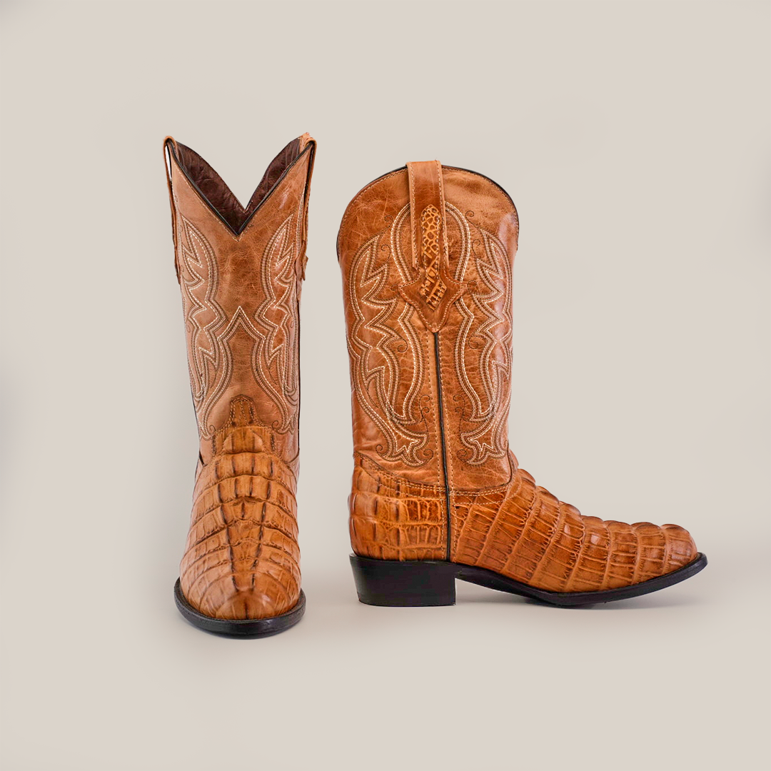 The Crocodile Tail Print Orix - Round Toe boots are handcrafted cowboy boots made from premium cowhide leather with intricate shaft stitching. These exotic brown boots, featuring a crocodile tail print, are displayed on a white background with one boot front-facing and the other side-facing.