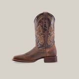 The Azkar Tan - Square Toe boot is a single rustic brown cowboy boot with detailed embroidery and a slightly worn finish on a white background. Made from premium cowhide leather, it features traditional Western design, artisanal excellence, a thick heel, and pointed toe.