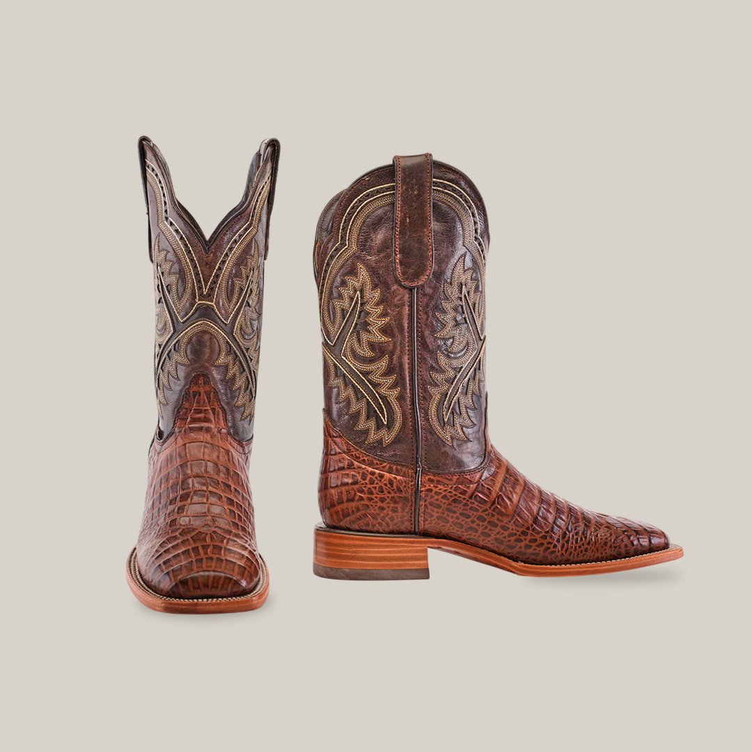 The Caiman Belly Print Chocolate boots feature intricate brown leather patterns with ornate embroidery. The left boot showcases a front square toe, while the right shows a side profile. Both have a wooden heel, set against a plain white background.