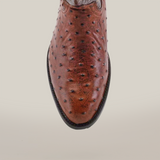 The Karoo Ostrich Print Chocolate - Round Toe boot, showcasing its luxury leather with distinctive texture and dark-edged sole, stands out against a white background.