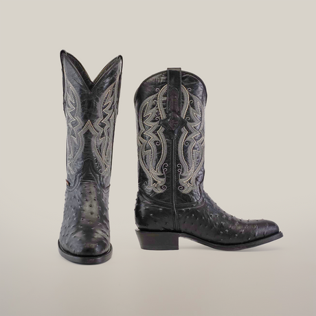 The Karoo Ostrich Print Black boot features intricate white stitching and decorative patterns on ostrich print leather. It elegantly stands out against a plain white background with its classic round toe and stacked heel.