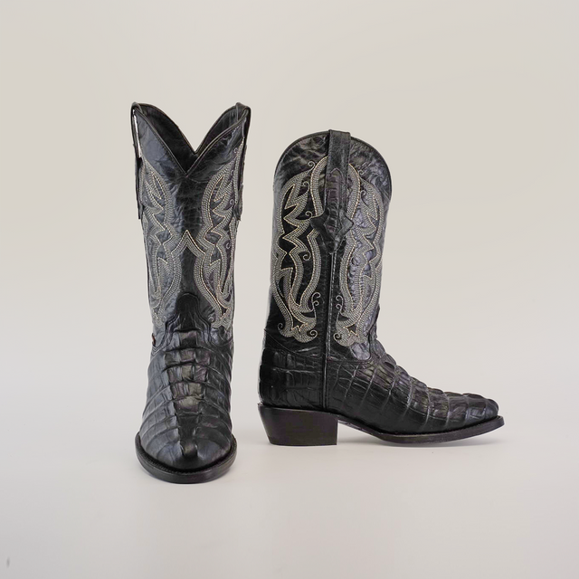 The Crocodile Tail Print Black cowboy boots feature a round toe and are handcrafted from black cowhide leather with intricate silver embroidery on the shafts. These boots have a textured, glossy finish set against a plain white background.