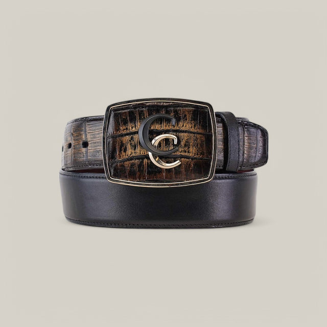 The Black & Brown Caiman Exotic Strip Belt - BC322 features luxurious dark leather coiled with a large square buckle. The buckles textured, earthy pattern showcases a stylish overlapping G and C metallic design on a neutral beige background, enhancing the exotic allure.