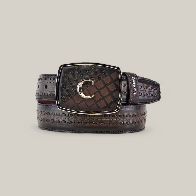 The Over Black Laser & Woven Belt - BC248 is neatly coiled, featuring dark brown leather with embossed patterns and a large rectangular buckle. A metallic C logo sits on a textured, checkered background, and the Cuadra brand name is embossed near the buckle, highlighting its distinct style.