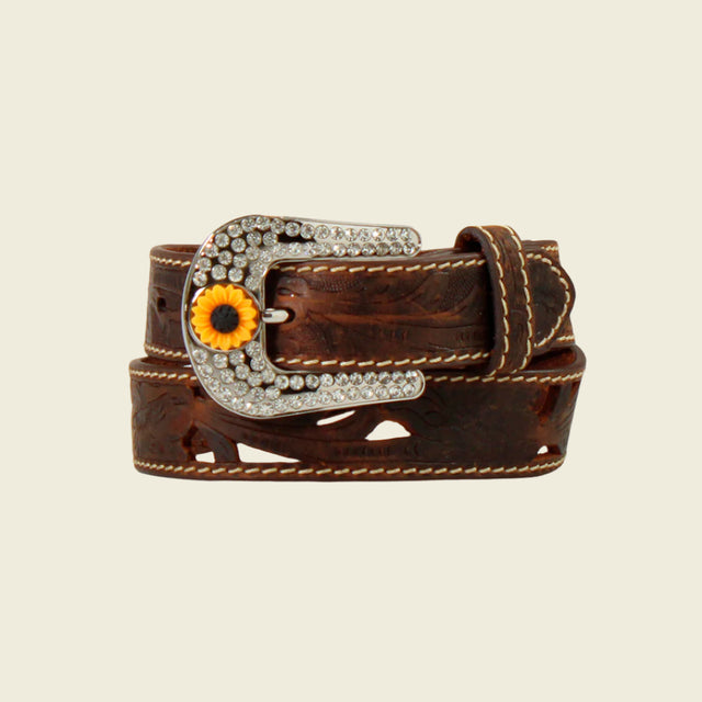 The Angel Ranch Western Girls Belt in brown (D130004002) features decorative stitching, a large silver buckle with sparkling gems, and a sunflower detail. Perfect for cowgirls, it epitomizes Western flair. The belt is rolled up against a light backdrop.