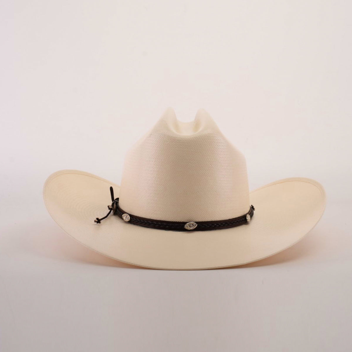 The 1000X Sinaloa Straw Hat boasts a wide brim and black braided band with silver conchos, elegantly set against a simple light backdrop.