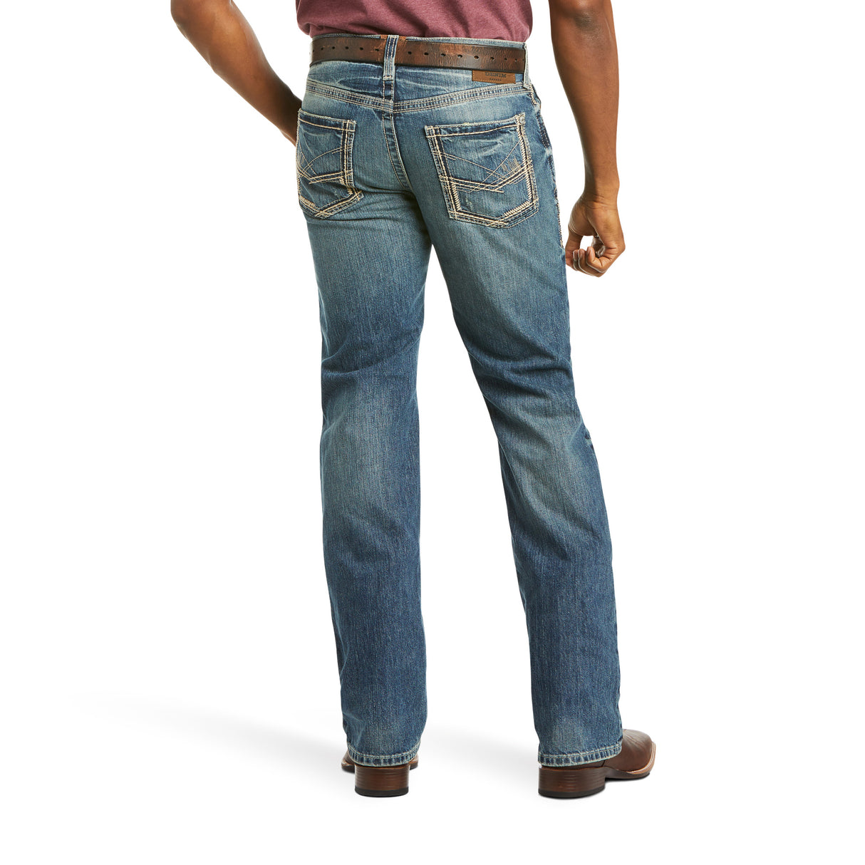 View of a person wearing the M5 Slim Gambler Stackable Straight Leg Jeans (10012703) with stitched back pockets, a brown belt, and brown shoes. The durable denim enhances their silhouette as they stand confidently with their left hand on their hip against a white background.