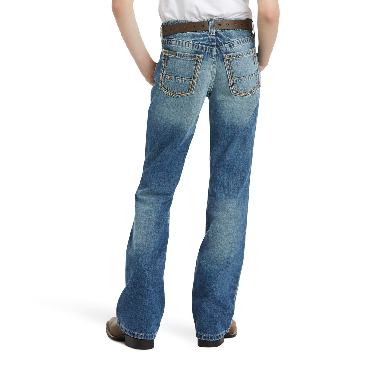 Rear view of a person in an Ariat Boys B4 Boundary Dakota bootcut jeans with brown stitching, hands in pockets. Featuring two back pockets and paired with brown shoes, the scene is set against a plain white background.