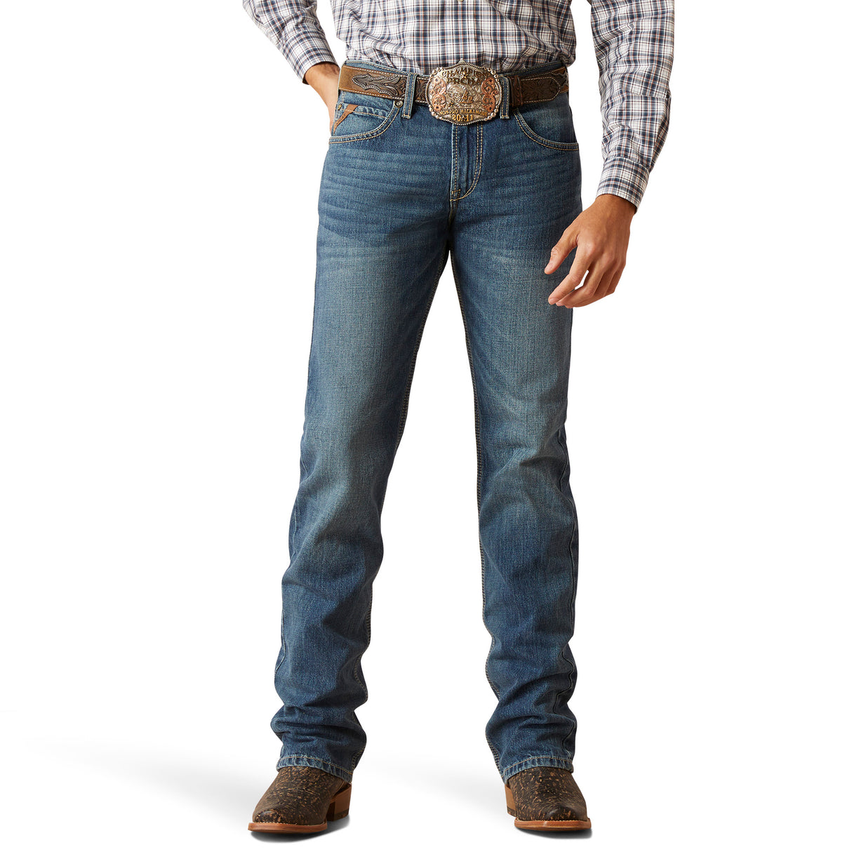 Dressed in the M7 Slim Ezra Straight Jean - Brighton, a person stands with hands at sides. The jeans have a slightly faded look, ideal for a modern cowboy, paired with brown cowboy boots and a large decorative belt buckle.