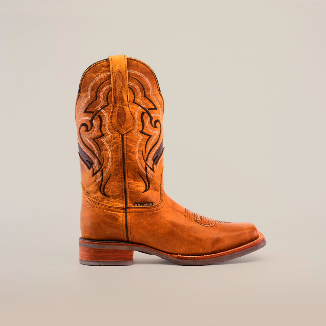 The Wild Mustard boot features decorative stitching on premium cowhide leather with a slightly worn texture and a wooden heel. This single brown cowboy boot is set against a plain white background.