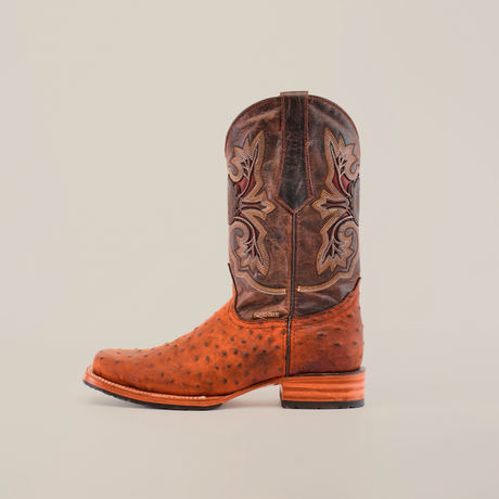 The Karoo Ostrich Roughout Print Cognac boot features a Rodeo toe, textured lower, and dark leather upper with intricate embroidery. Highlighted against white, it showcases a slip-resistant sole.