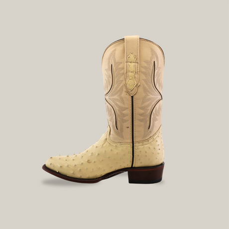 A single Exotic Full Quilt Ostrich Boot in bone, featuring genuine ostrich leather and intricate stitching on the shaft. This handcrafted boot by skilled artisans is presented against a plain light gray background, emphasizing its squared-off heel.