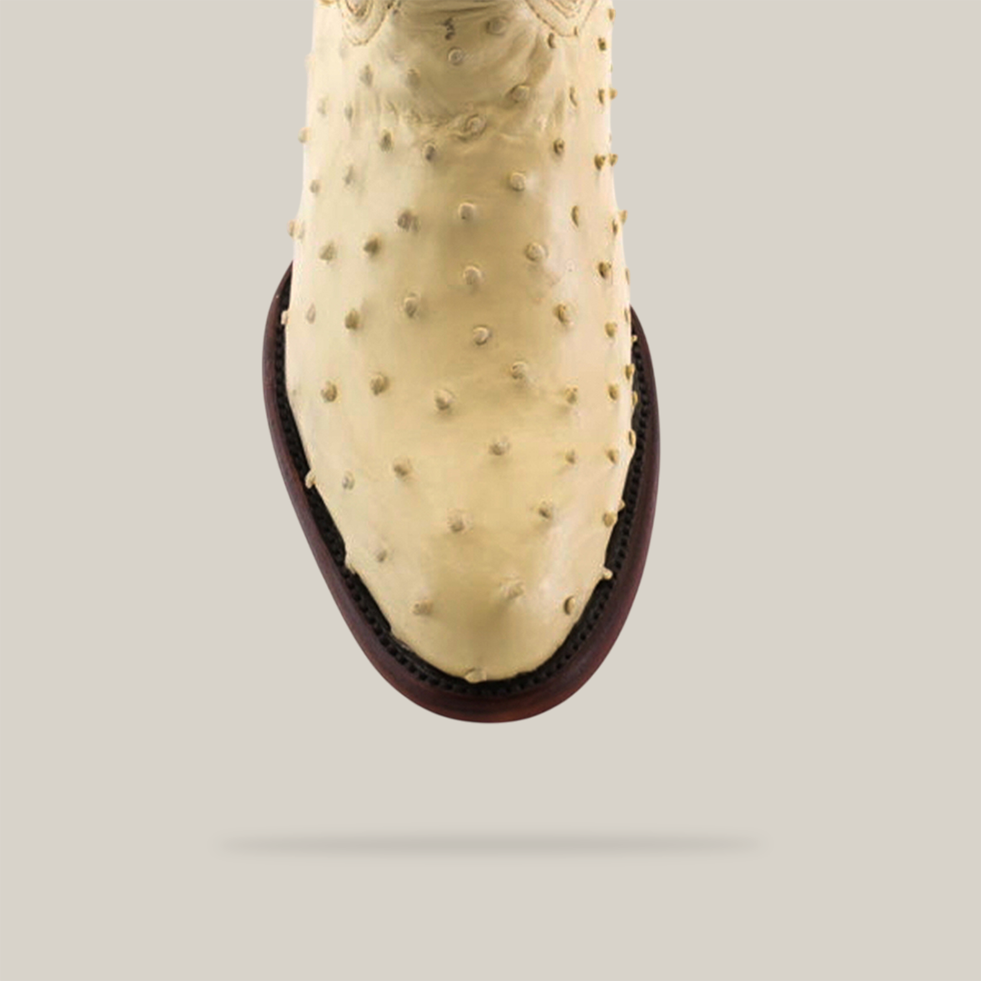 Top view of a single handcrafted Exotic Full Quilt Ostrich - Bone boot with visible texture, featuring dark brown stitching around the sole, set against a light gray background.