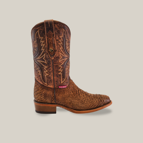 Exotic Python - Tamarindo: Brown cowboy boot crafted from textured leather with detailed stitching on the shaft. It features a round toe, small heel, and pink side label. Displayed against a light beige background, this design embodies Western heritage nodding to classic style.