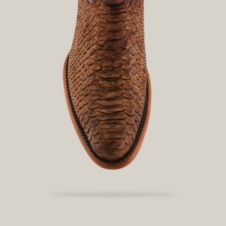 Top view of a single brown Exotic Python - Tamarindo cowboy boot on a light beige background. The round toe boot showcases an exotic python-like pattern and detailed stitching along the edges, casting a soft shadow below, embodying western heritage charm.