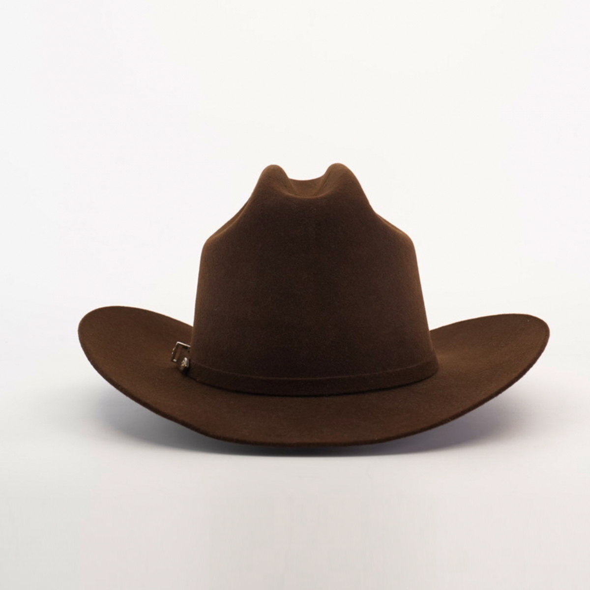 The 6X 2 Carnales Brown cowboy hat, with a wide brim and slightly creased crown, rests on a white surface. This classic western piece is crafted from durable sheep wool felt and finished with a simple band encircling the base for a timeless look.