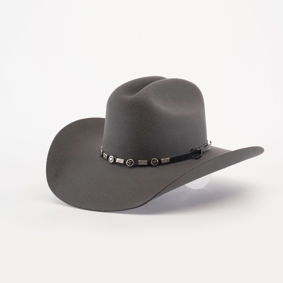 The 6X Dallas Oxford is a wide-brimmed dark gray felt hat with a dented crown and a decorative hatband adorned with circular metal accents, exuding Western sophistication as it rests elegantly on a white surface.