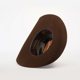 The 6X Dallas Brown felt hat is displayed on its side, highlighting its Western sophistication with visible interior lining and branding. Its distinctive shape and rich color stand out against the plain white background, making it ideal for those seeking classic cowboy charm.